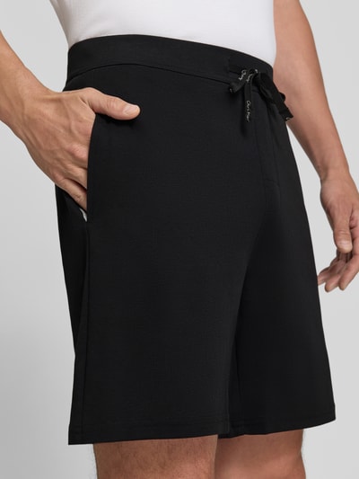 Männermodel trägt schwarze Sweatshorts aus reiner Baumwolle von Christian Berg Men, elastischer Bund, Label-Details, Nahaufnahme Oberkörper.