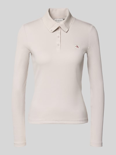 Frauenmodel trägt Slim Fit Langarmshirt aus Baumwoll-Mix von Calvin Klein Jeans in Creme mit feiner Struktur und kleinem Logo, Ganzkörperansicht von vorne.