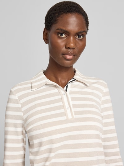 Frauenmodel trägt Longsleeve im Allover-Look mit Polokragen und Knopfleiste von Marc Cain, beige-weiße Streifen, schimmernd, Nahaufnahme Oberkörper. Material-Mix mit Stretch-Anteil, Regular Fit.