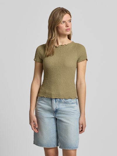 Frauenmodel trägt Slim Fit T-Shirt mit Strukturmuster Modell 'Alora' von Noisy May in Olivgrün, leichte Textur, U-Boot-Ausschnitt, Kurzarm, kombiniert mit hellblauer Shorts, Ganzkörperansicht von vorne.