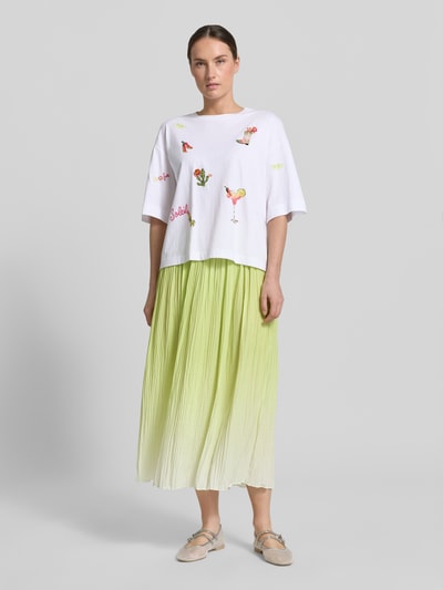 Modelka nosi T-Shirt mit Motiv-Stitchings od Marc Cain z czystej bawełny, krój loose fit, okrągły dekolt, aplikacje z cekinami, długość tyłu w rozmiarze 36: 55 cm, białe z kolorowymi wyszywaniami na gładkim tle, widok całej sylwetki z przodu.