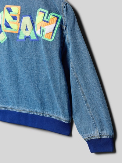 Mädchen trägt Jeansjacke mit rückseitigem Statement-Stitching von BILLIEBLUSH, bunte Buchstaben, blaue Ärmel, Nahaufnahme Rückansicht, Material-Mix mit Stretch-Anteil, Loose Fit, gerippte Abschlüsse.