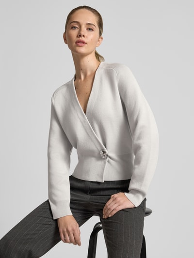 Frauenmodel trägt Cardigan im Wickel-Look - curated by Isabelle Hartmann von Style Icon Collection, Lockerer-Schnitt, V-Ausschnitt, Knopfverschluss, gerippte Ärmelabschlüsse, Hellgrau, feine Stricktextur, Ganzkörperansicht von vorne.