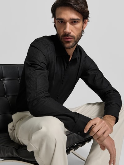 Männermodel trägt Slim Fit Freizeithemd aus reiner Baumwolle Modell 'KENNO' von HUGO in Schwarz, feines Strukturmuster, Nahaufnahme Oberkörper.
