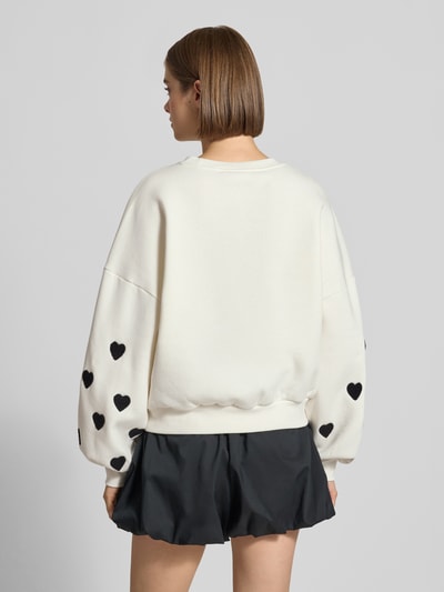 Frauenmodel trägt Regular Fit Sweatshirt aus Baumwoll-Mix Modell 'MACY' von ONLY, cremefarben mit schwarzen Herzen, Damen Sweatshirt von ONLY, Ganzkörperansicht Rückansicht.