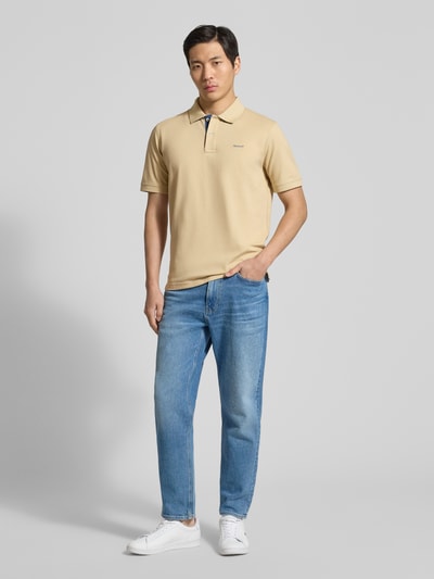 Männermodel trägt Regular Fit Poloshirt mit Logo-Stitching von Gant in Beige, elastischer Baumwoll-Mix, klassischer Polokragen, Ganzkörperansicht von vorne.
