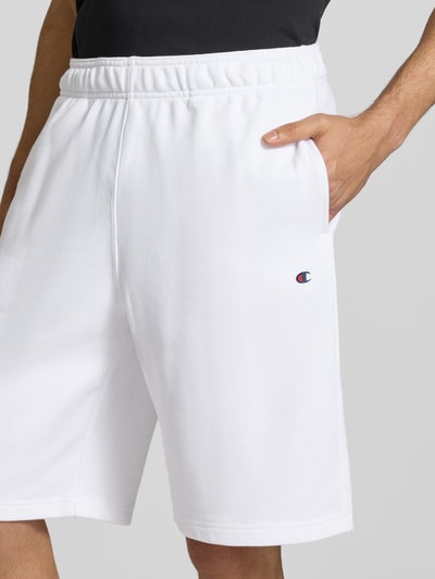Männermodel trägt weiße Shorts mit Logo-Print und -Stitching von CHAMPION, Baumwoll-Mix, lockerer Schnitt, Nahaufnahme Oberkörper.