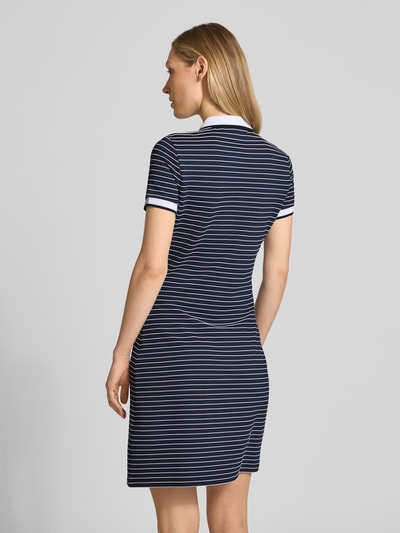 Männermodel trägt knielanges Polokleid mit Polokragen Modell 'ALPHONSINE' von Guess, krój slim fit, viskoza z dodatkiem stretchu, długość do kolan, krótka listwa guzikowa, miękka tekstura, granatowo-białe paski, Szerokość w rozmiarze S: 40 cm, długość tyłu: 93 cm, długość rękawa: 18 cm, Ganzkörperansicht Rückansicht