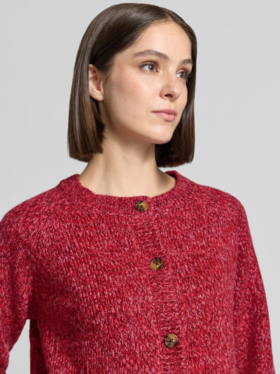 Frauenmodel trägt Relaxed Fit Strickjacke aus Woll-Mix Modell 'Nova' von LOLLYS LAUNDRY in meliertem Rot mit Knopfleiste, Nahaufnahme Oberkörper, Damen Strickjacke Woll-Mix, langärmlig, Rückenlänge 52 cm, Ärmellänge 47 cm.