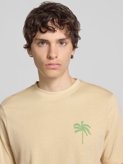 Männermodel trägt T-Shirt mit Motiv-Print Modell 'SUN PALMS' von Blend in Beige mit grünem Palmenprint, reine Baumwolle, Nahaufnahme Oberkörper.