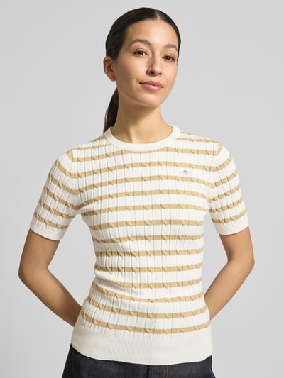 Frauenmodel trägt Strickshirt mit Rundhalsausschnitt und Label-Stitching von Gant, Slim Fit im Ripp-Design, cremeweiß mit beigen Streifen, Baumwoll-Mix mit Stretch-Anteil, Nahaufnahme Oberkörper.