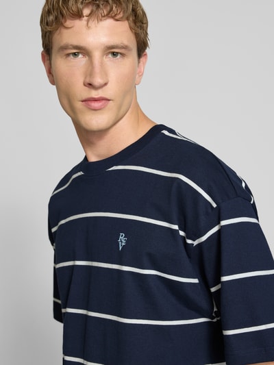Männermodel trägt T-Shirt mit Rundhalsausschnitt und Logo-Stitching von REVIEW, Reine Baumwolle, Loose-Fit, Nahaufnahme Oberkörper.