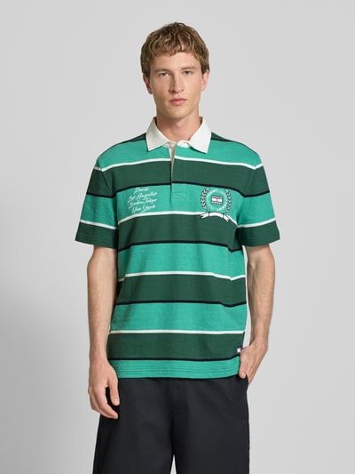 Männermodel trägt Regular Fit Poloshirt aus reiner Baumwolle von Tommy Jeans in Two-Tone-Optik mit Label-Print, Motiv-Print, Jersey-Textur, Ganzkörperansicht von vorne.