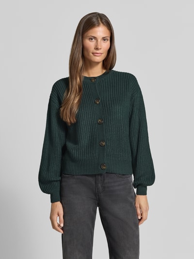 Frauenmodel trägt dunkelgrüne Loose Fit Strickjacke mit einreihiger Knopfleiste Modell 'LEA' von VERO MODA, gerippte Textur, Ganzkörperansicht von vorne. Damen Strickjacke von VERO MODA.