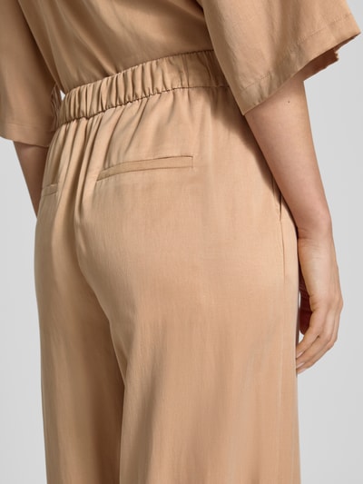 Frauenmodel trägt Wide Fit Stoffhose mit elastischem Bund Modell 'Consider' von Drykorn, Cupro-Mix, beige, glatte Textur, Detailaufnahme Rückansicht.