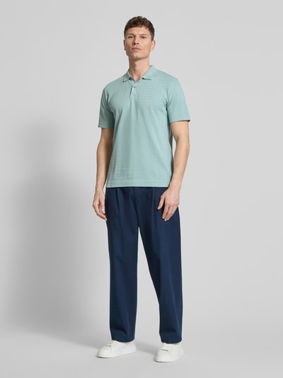 Männermodel trägt Regular Fit Poloshirt aus reiner Baumwolle von Marc O'Polo in Mint, Gitterkaro Struktur, Ganzkörperansicht von vorne.