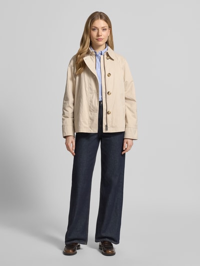 Vrouwenmodel draagt Jacke mit seitlichen Eingrifftaschen und Kentkragen van Fuchs Schmitt in beige, recht model, kentkraag, knoopsluiting, raglanmouwen, steekzakken, ruglengte bij maat 36: 64 cm, schouderbreedte: 38 cm, borstwijdte: 51 cm, mouwlengte: 44 cm, full-body vooraanzicht.