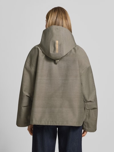 Frauenmodel trägt Regular Fit Jacke mit Kapuze Modell 'Elle' von G-LAB in Oliv mit Druckknopfverschluss, Tunnelzug, Eingrifftaschen, Rückenlänge 64 cm, Schulterbreite 56 cm, Brustweite 56 cm, Ärmellänge 51 cm, Ganzkörperansicht Rückansicht.