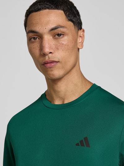 Männermodel trägt Regular Fit Sport-T-Shirt mit Logo-Print Modell 'WE BAS T' von adidas in Grün, adidas Training, Nahaufnahme Oberkörper.