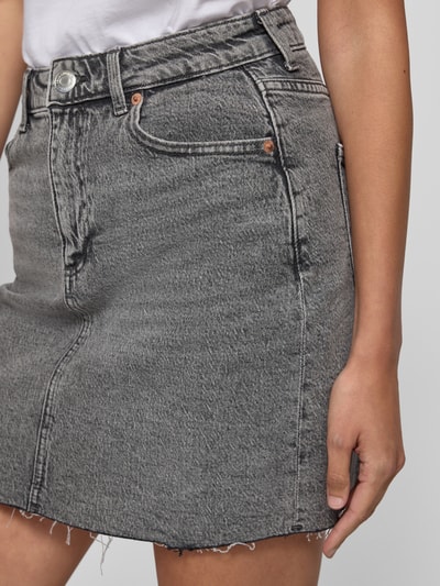 Vrouwenmodel draagt Regular Fit jeansrok uit katoenmix model 'TESSA' van Vero Moda in grijze denimlook met labelpatch, 5-pocketmodel, knoop- en ritssluiting, twill structuur en minilengte, detailopname bovenbeen.