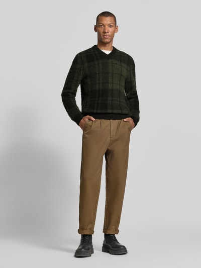 Männermodel trägt Pullover mit weichem Wollmix von BARBOUR in Strickoptik, kariert, mehrfarbig, V-Ausschnitt, Ganzkörperansicht von vorne.