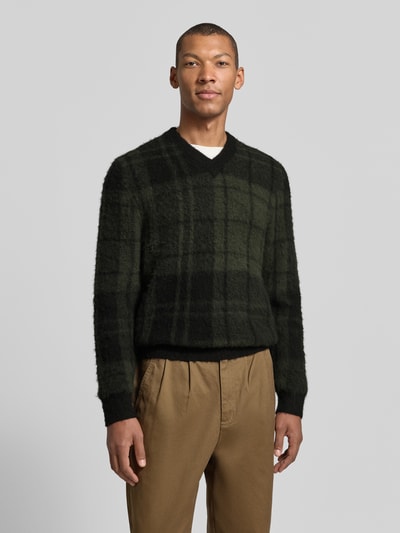 Männermodel trägt Pullover mit weichem Wollmix von BARBOUR, Strickoptik kariert in Grün und Schwarz, V-Ausschnitt, Nahaufnahme Oberkörper.