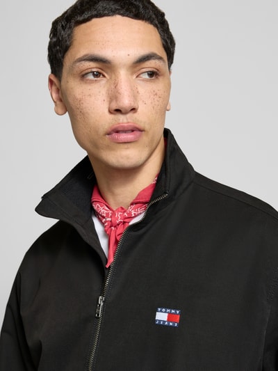 Männermodel trägt Regular Fit Blouson van Tommy Jeans in effen zwart met label patch, staande kraag, rits, elastische boorden, zijkantzakken, Nahaufnahme Oberkörper.