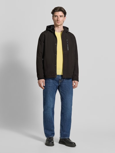 Męski model nosi Jacke mit Napoleontasche Modell 'KOS' od Killtec w kolorze czarnym, krój regular fit, przód, zdjęcie całopostaciowe. Kurtka z kapturem ze ściągaczem, pełny zamek z listwą, napoleońska kieszeń, regulowane mankiety, naszywka z logo, długość tyłu w rozmiarze M: 73 cm, szerokość ramion w rozmiarze M: 46 cm, szerokość w klatce piersiowej w rozmiarze M: 60 cm, długość rękawa w rozmiarze M: 71 cm.