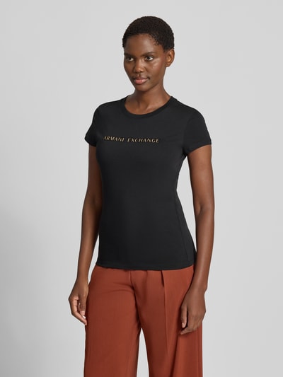 Kobiece modelka nosi czarny Damski t-shirt 'Slim Fit T-Shirt aus reiner Baumwolle' od Armani Exchange z detalem z logo, okrągły dekolt, bawełna, krój slim fit, długość tyłu w rozmiarze S: 59 cm, widok całej sylwetki z przodu.