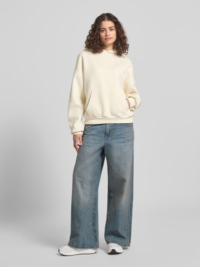 Frauenmodel trägt Relaxed Fit Sweatshirt mit Logo-Print von Review, cremefarben, Känguru-Tasche, elastische Abschlüsse, Ganzkörperansicht von vorne.