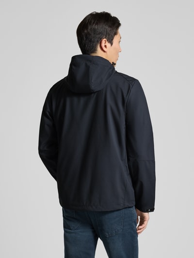 Męski model nosi Regular Fit Jacke mit mit Logo-Applikation von Killtec, czarny kolor, kaptur z troczkiem, kieszenie zapinane, krój regular fit, długość tyłu w rozmiarze M: 72 cm, szerokość ramion w rozmiarze M: 45 cm, szerokość klatki piersiowej w rozmiarze M: 57 cm, długość rękawa w rozmiarze M: 67 cm, widok całej sylwetki z tyłu.
