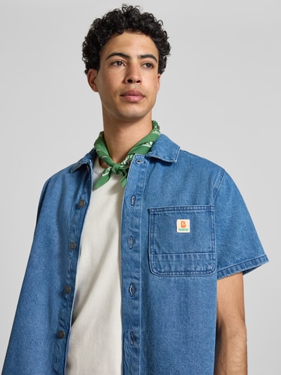 Männermodel trägt Regular Fit Jeanshemd mit Brusttasche Modell 'SUN' von Blend, reine bawełna, kołnierzyk typu kent, listwa guzikowa, naszywka z logo, brustasza, długość tyłu w rozmiarze M: 70 cm, szerokość ramion w rozmiarze M: 42 cm, długość rękawów w rozmiarze M: 23 cm, niebieski denim o gładkiej fakturze, nahaufnahme oberkörper
