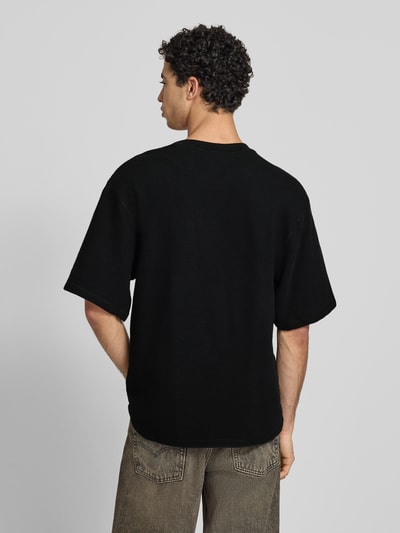 Männermodel trägt Relaxed Fit T-Shirt mit Strukturmuster von KARL KANI in Schwarz aus reiner Baumwolle, Logo-Stitching, Rundhalsausschnitt, Rückenlänge bei Größe M 71 cm, Ganzkörperansicht Rückansicht.