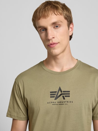 Männermodel trägt T-Shirt mit Logo und Rundhalsausschnitt von Alpha Industries aus Reine Baumwolle, Regular-Fit, Logo, Nahaufnahme Oberkörper.