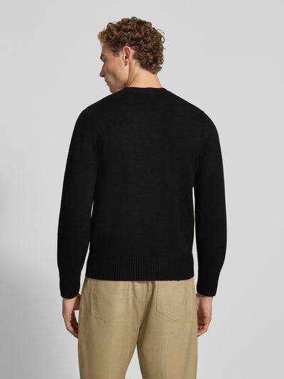 Männermodel trägt Regular Fit Pullover aus reiner Wolle von Lacoste in Schwarz, beige Hose, Ganzkörperansicht Rückansicht. Herren Pullover von Lacoste