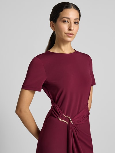 Frauenmodel trägt Midikleid mit Zierschnalle Modell 'Justine' von VILA in Bordeaux, elastischer Material-Mix, taillierte Passform, Kurzärmeliges Design, Rundhalsausschnitt, Nahaufnahme Oberkörper.