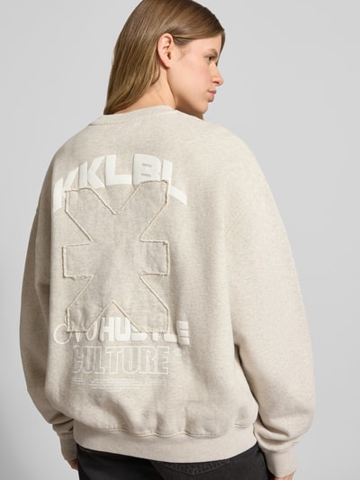 Frauenmodel trägt Sweatshirt mit rückseitigem Statement-Print Modell 'No Hustle' von Karo Kauer aus Reine Baumwolle, Oversized-Fit, beige mit Logo-Print und gerippte Abschlüsse, Ganzkörperansicht Rückansicht.