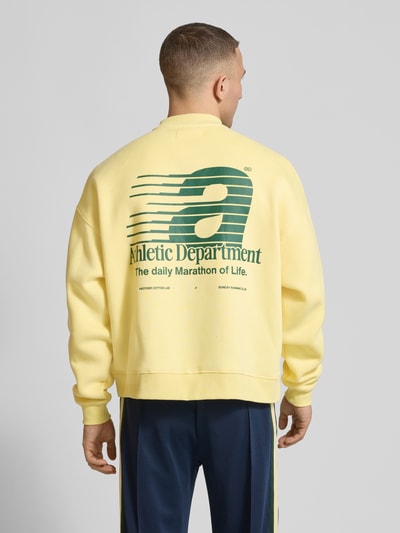Männermodel trägt Sweatshirt mit Statement-Prints Modell 'Athletic Department' von ANOTHER COTTON LAB in Gelb, Baumwoll-Mix, lockere Passform, gerippter kurzer Stehkragen, überschnittene Schultern, grüne Prints auf dem Rücken, Rückenlänge 67 cm, Ganzkörperansicht Rückansicht