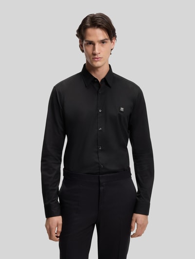 Männermodel trägt Slim Fit Freizeithemd aus Baumwoll-Mix Modell 'ERMO' von HUGO in Schwarz mit Kentkragen und Label Patch, Ganzkörperansicht von vorne.