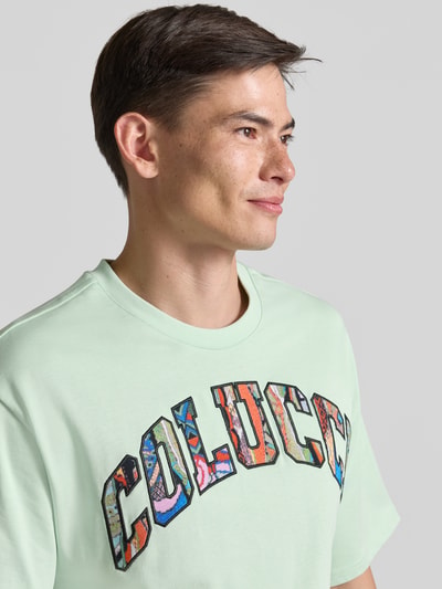 Männermodel trägt T-Shirt mit 1/2-Arm von COLUCCI in Mintgrün mit buntem Logo, reine Baumwolle, gerader Schnitt, Nahaufnahme Oberkörper.