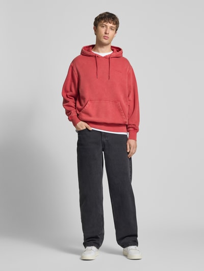 Männermodel trägt Hoodie mit Label-Stitching und Känguru-Tasche von Dickies in Rot, Relaxed Fit, Baumwoll-Mix, Ganzkörperansicht von vorne.