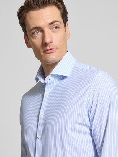 Männermodel trägt Slim Fit Business-Hemd mit Haifischkragen von Seidensticker im hellblau-weißem Streifenmuster, Material-Mix mit Stretch-Anteil, Knopfleiste, Nahaufnahme Oberkörper.