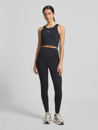 Frauenmodel trägt Cropped Tanktop mit Logo von Salomon aus Material-Mix mit Stretch-Anteil, Schwarz, Rundhalsausschnitt, Ganzkörperansicht von vorne. Rückenlänge bei Größe S: 35 cm.