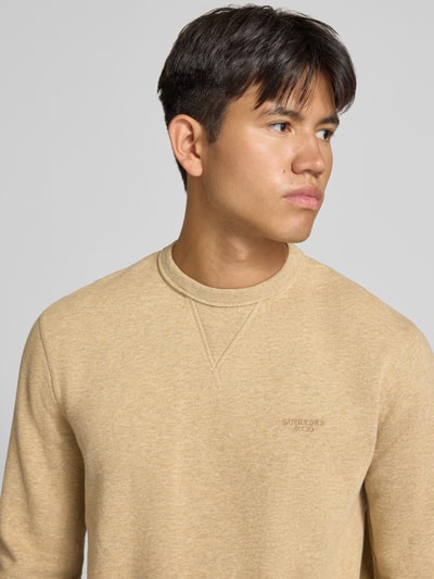 Männermodel trägt Sweatshirt aus Baumwoll-Mix von Superdry in Beige mit Label-Stitching, lockerer Passform, Nahaufnahme Oberkörper.