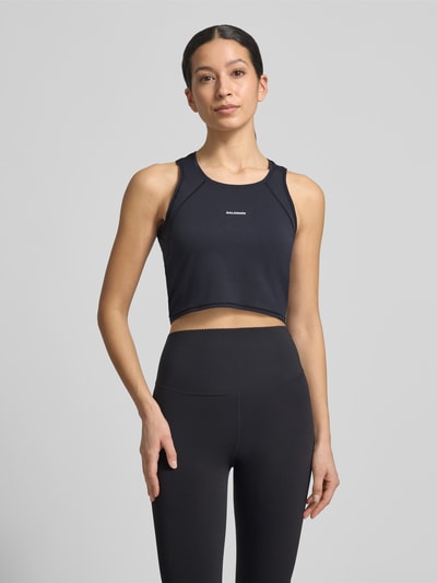 Frauenmodel trägt Cropped Tanktop mit Logo von Salomon aus schwarzem Material-Mix mit Stretch-Anteil, Rundhalsausschnitt, Ganzkörperansicht von vorne. Rückenlänge bei Größe S: 35 cm.