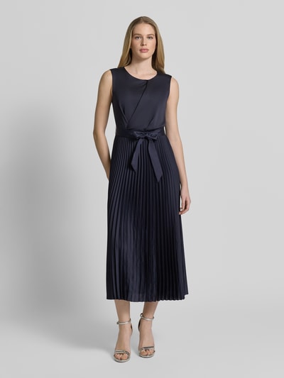 Modelka kobieca nosi 'Cocktailkleid mit Plisseefalten' od Vera Mont, kolor granatowy, tkanina z plisami, pasek w talii, długość midi, krój slim fit, okrągły dekolt, suwak z tyłu, szerokość w rozmiarze 36: 30 cm, długość tyłu: 126 cm, widok całej sylwetki z przodu.