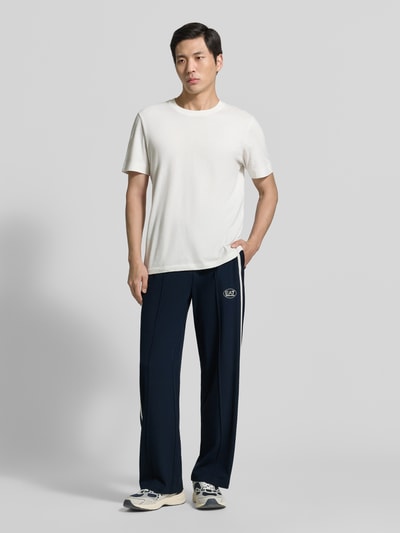 Mannelijk model draagt trainingsbroek uit viscosemix van EA7 Emporio Armani, recht pasvorm, galonstrepen, steekzakken, labelprint, binnenbeenlengte maat M 79 cm, mix van viscose en elastaan. Volledige lichaamsweergave van voren.