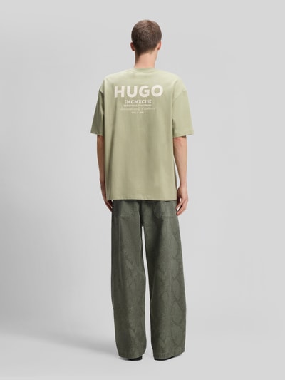 Männermodel trägt Relaxed Fit T-Shirts aus reiner Baumwolle von HUGO, helle Grüntöne, Matte Textur, Ganzkörperansicht Rückansicht. Herren Oversized Shirt von HUGO Blue.