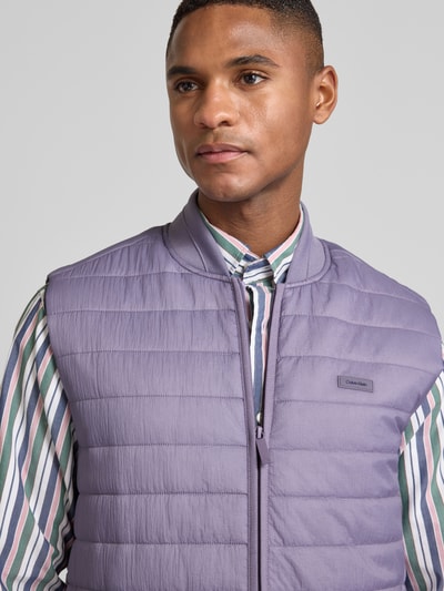 Männermodel trägt Steppweste mit Reißverschlusstaschen von CK Calvin Klein, glattes Material, Unifarbenes-Design, Label-Applikation, Nahaufnahme Oberkörper.