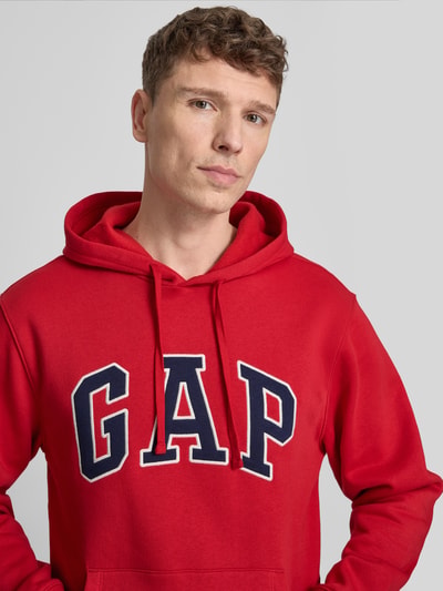 Männermodel trägt Hoodie met kangoeroezak van GAP in rood katoenmix met labelstitching, los model, Nahaufnahme Oberkörper.